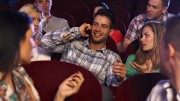Confident young man talking on mobilephone in cinema, spectators looking angry.
